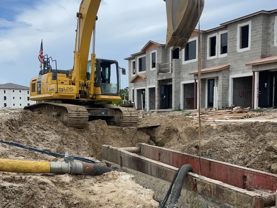 Tracked excavator digging a sewer-main trench next to a new residential build — Fort Myers, Florida