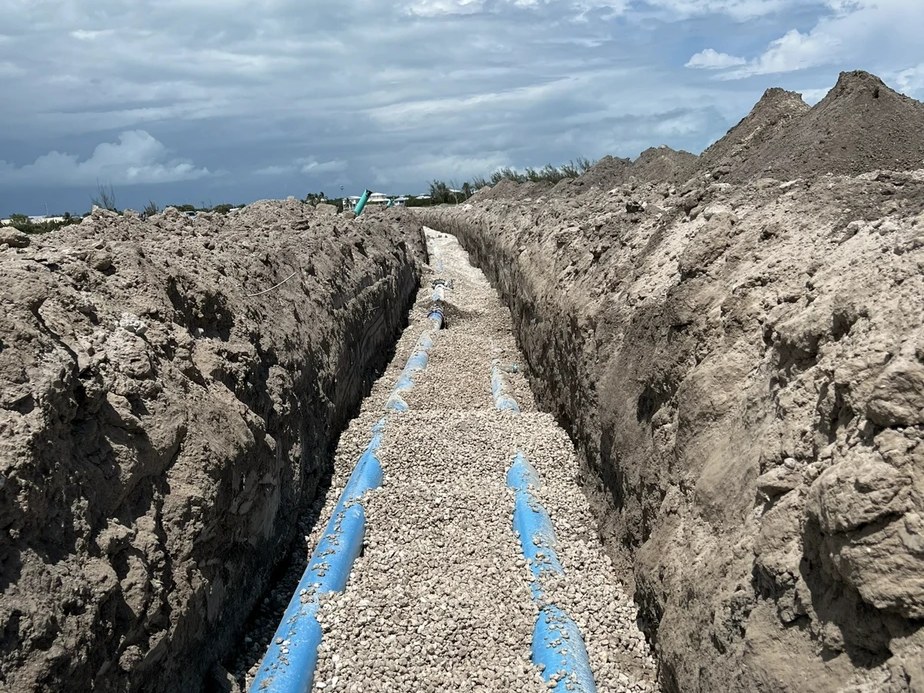 Water-main trench with newly laid blue pipes and finished grading — Marathon, Florida